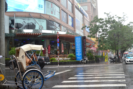 Pedicab driver huddles in rain waiting for customer.
