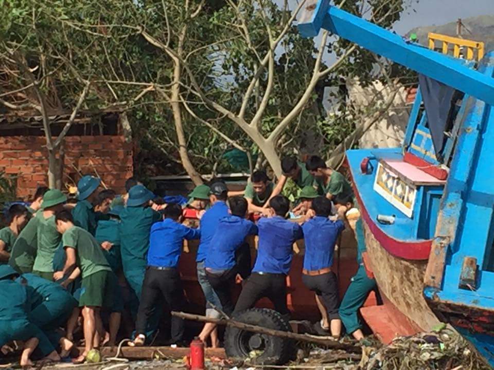 Bộ đội và thanh niên giúp dân đưa tàu cá bị sóng đánh dạt lên đất liền xuống biển