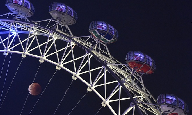 Siêu trăng đỏ ẩn hiện phía sau các cabin của vòng quay London Eye ở London, Anh. Ảnh: Reuters.
