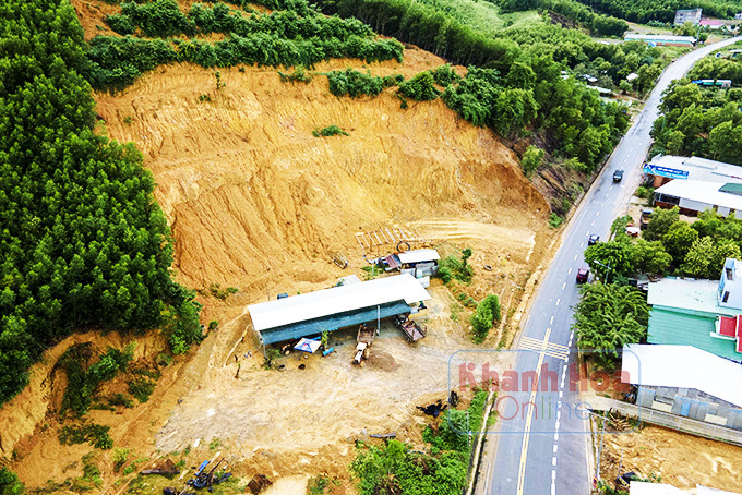 Vách đất cao hơn 10m hình thành ngay gần cổng chào  huyện Khánh Vĩnh, dưới chân đồi mọc lên một cơ sở  sửa chữa máy móc.