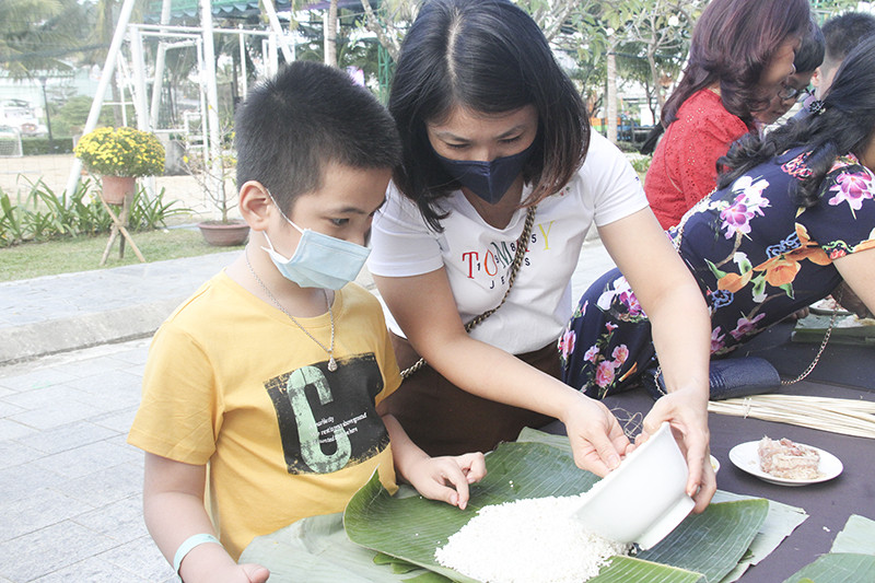 Một bà mẹ trẻ dạy con cách gói bánh Tét.