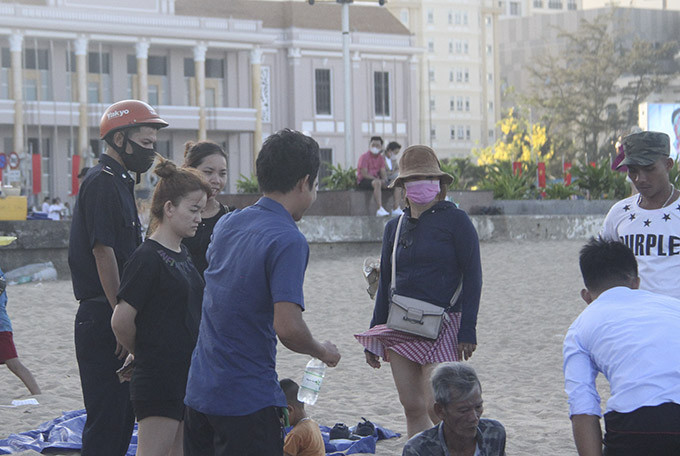 Lực lượng chức năng của TP. Nha Trang nhắc nhở một nhóm người không đeo khẩu trang khi chơi trên bãi biển