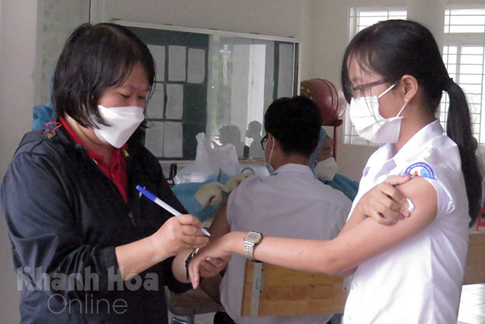 Medical staff making note of post-injection follow-up time for students of Le Quy Don Gifted High School 