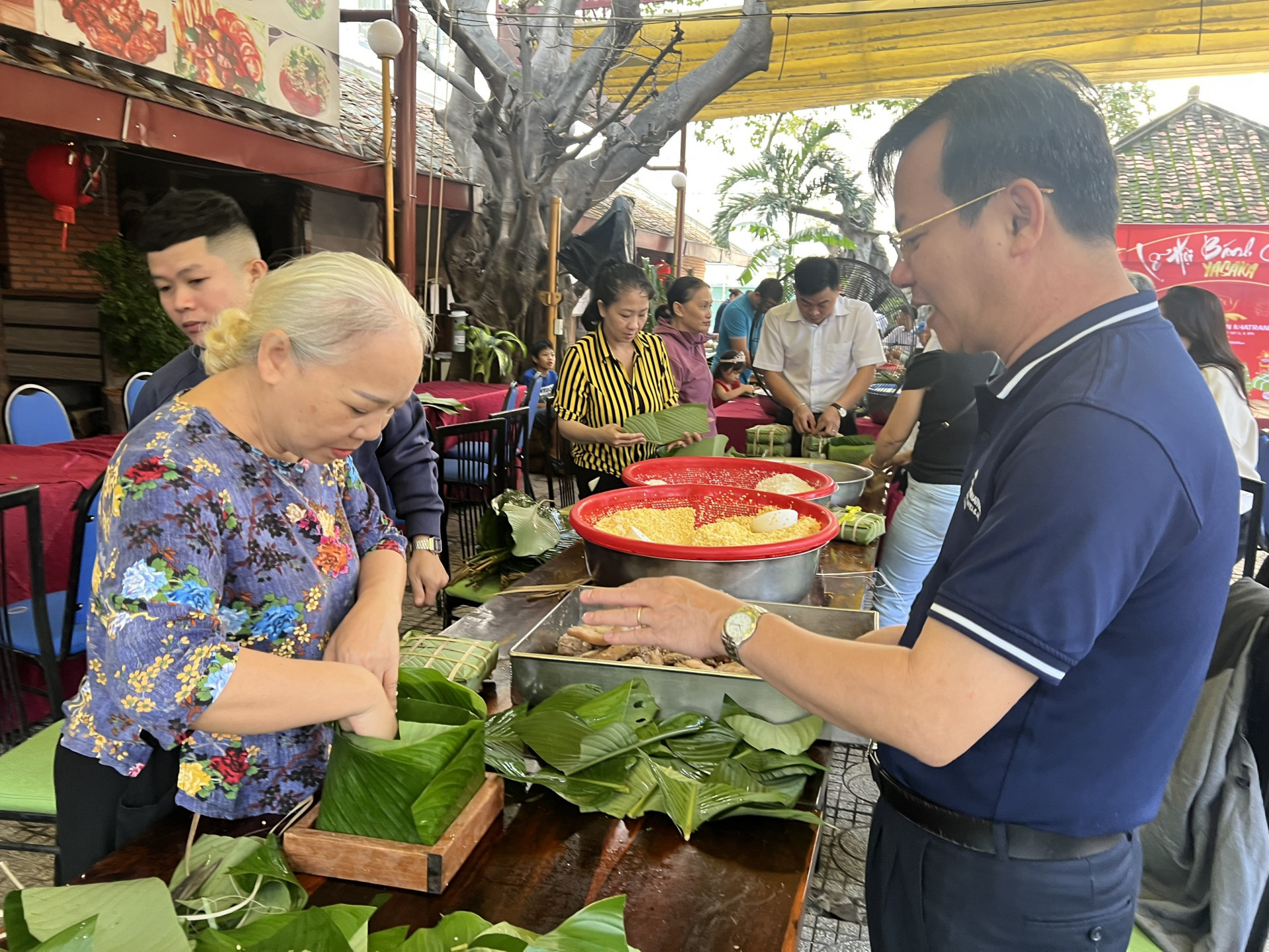 Bà Bích Thủy (70 tuổi, Nha Trang) tập gói bánh chưng dưới sự hướng dẫn của ông Trần Tấn Ngọc - Tổng Giám đốc Công ty Cổ phần Yasaka-saigon-Nhatrang